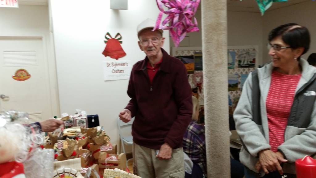 Two people stand beside a table of gifts and decorations in a festively decorated room.