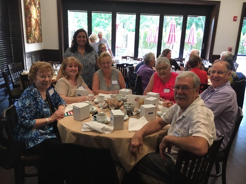 Group of people seated around a table at a restaurant, smiling and chatting over coffee cups and napkins.