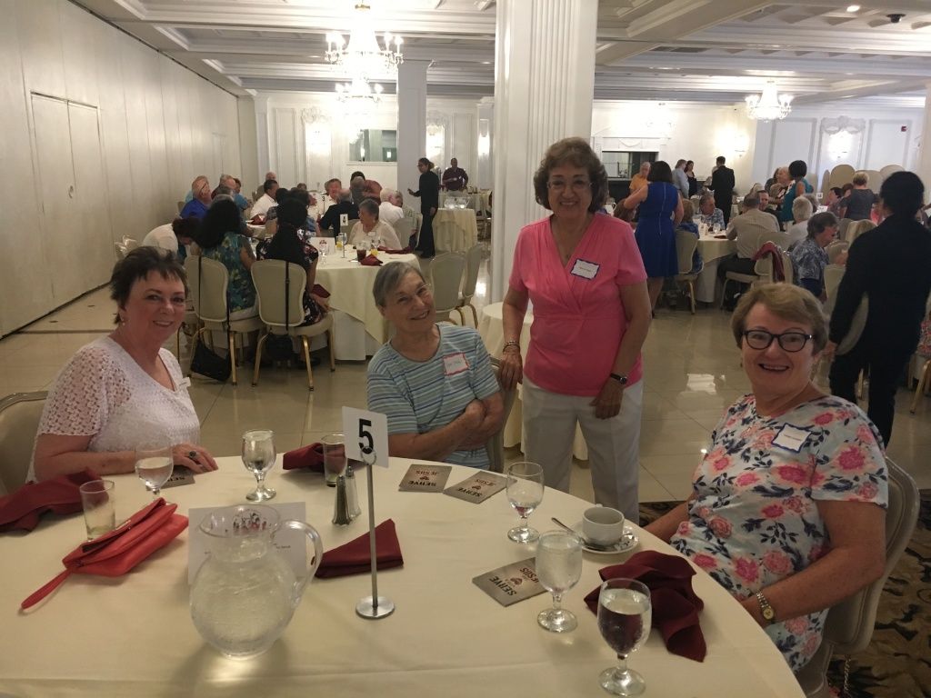 Group of people seated at round tables in a bright banquet hall, with a table number sign in the foreground.