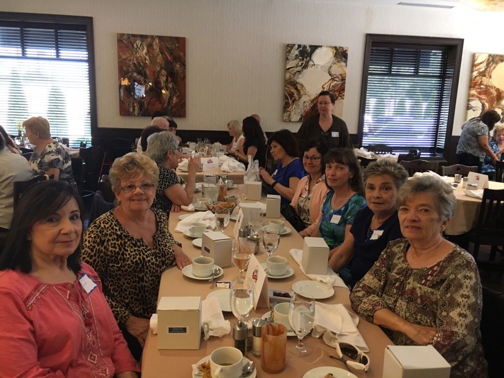Group of people seated at a long table in a bright dining room, chatting over tea and coffee.