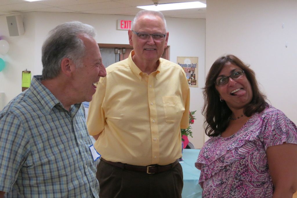 Three people smiling in a bright indoor hallway, standing and talking