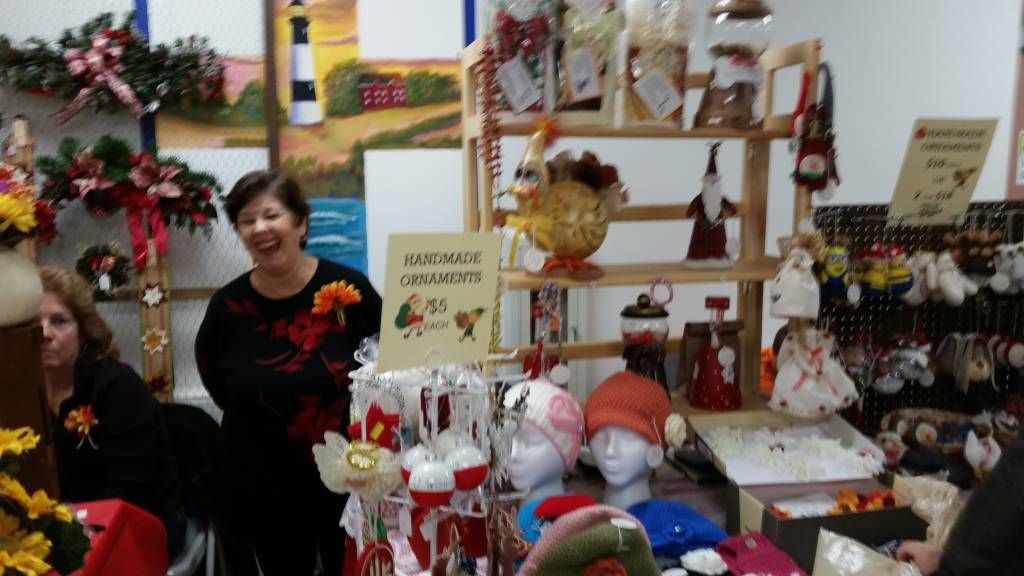 Two people at a festive craft stall with holiday decorations, ornaments, and handmade items displayed on shelves.