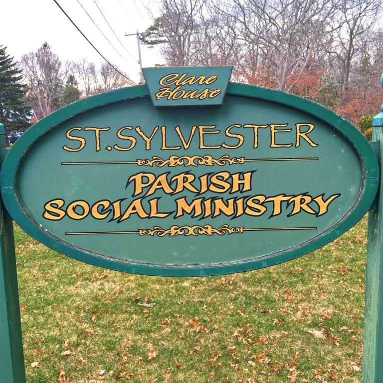 Green oval sign for St. Sylvester Parish Social Ministry, with “Clare Haven,” outdoors among trees.