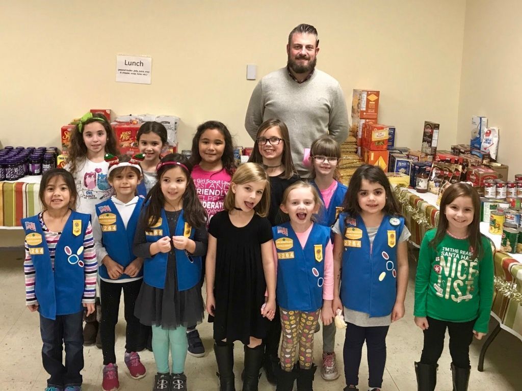 Children in blue vests stand with a man in a room filled with donated items.