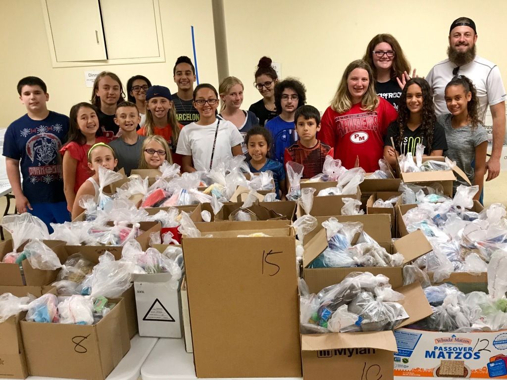 Group of volunteers standing behind tables covered with packed donation bags and boxes in a community room