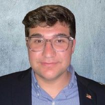 A young man wearing glasses and a suit is smiling for the camera.