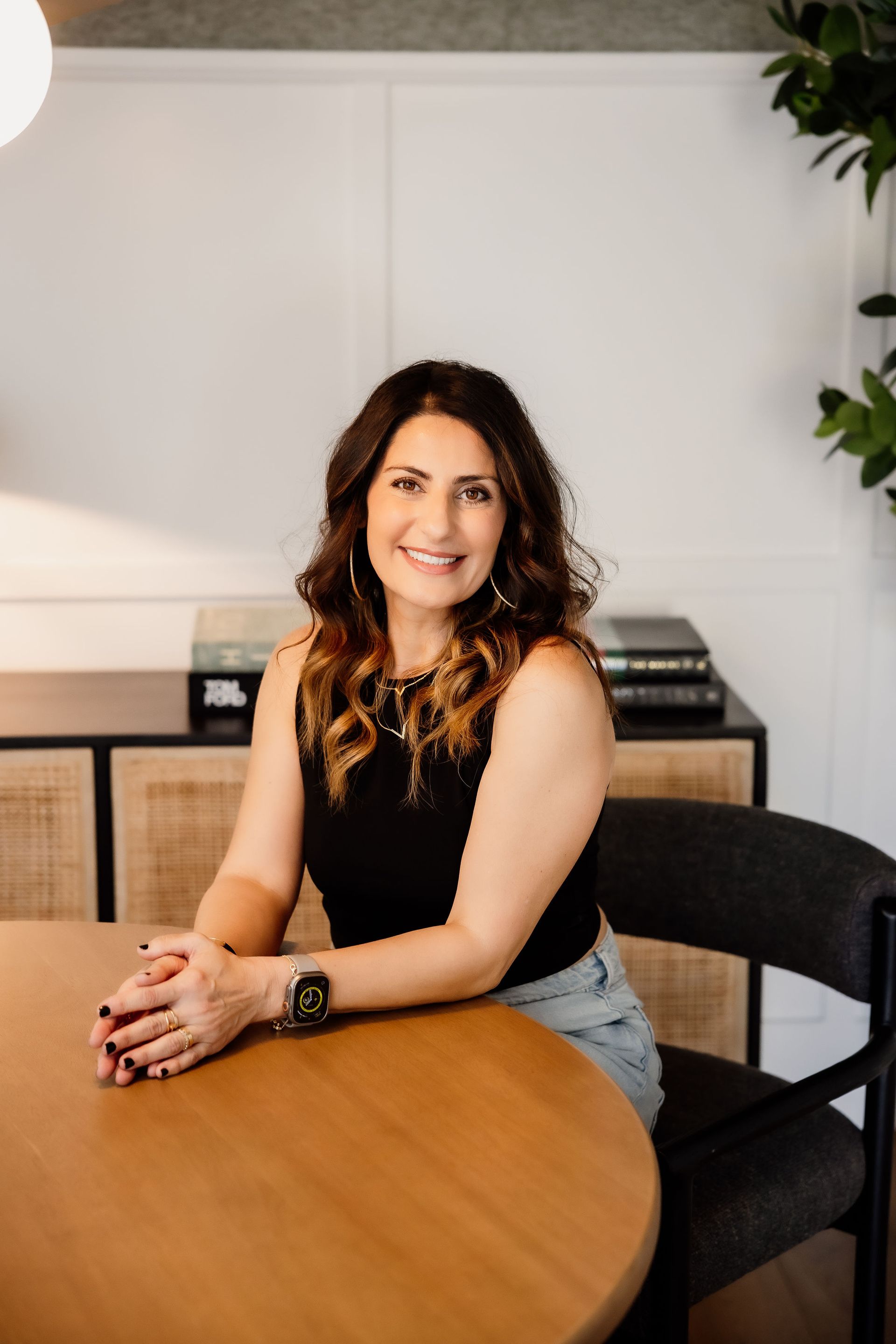 Mania Persekian, REALTOR, seated at a table in a bright office with a relaxed, professional pose.