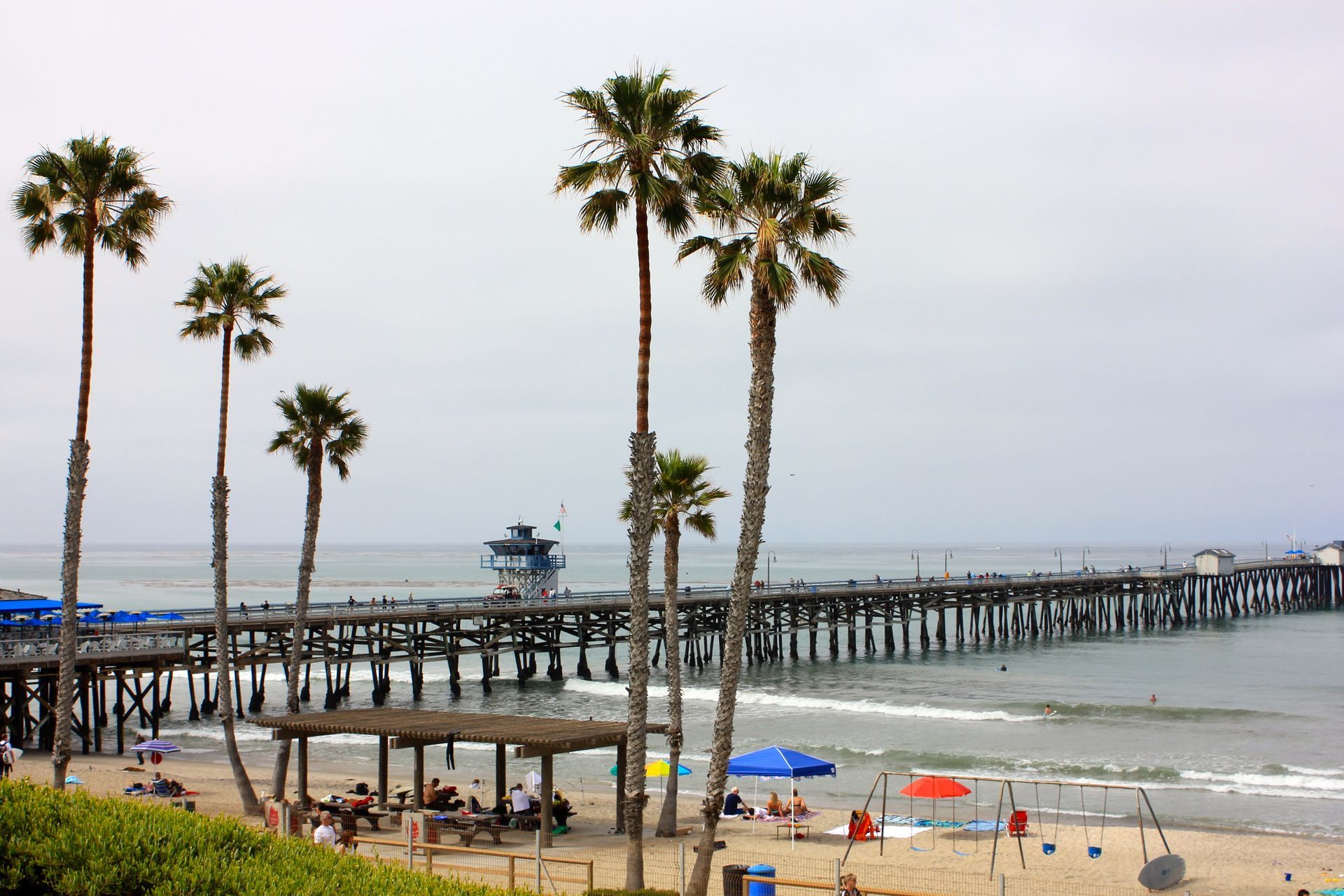 San Clemente pier and beach with palm trees and calm ocean waters on a clear day.