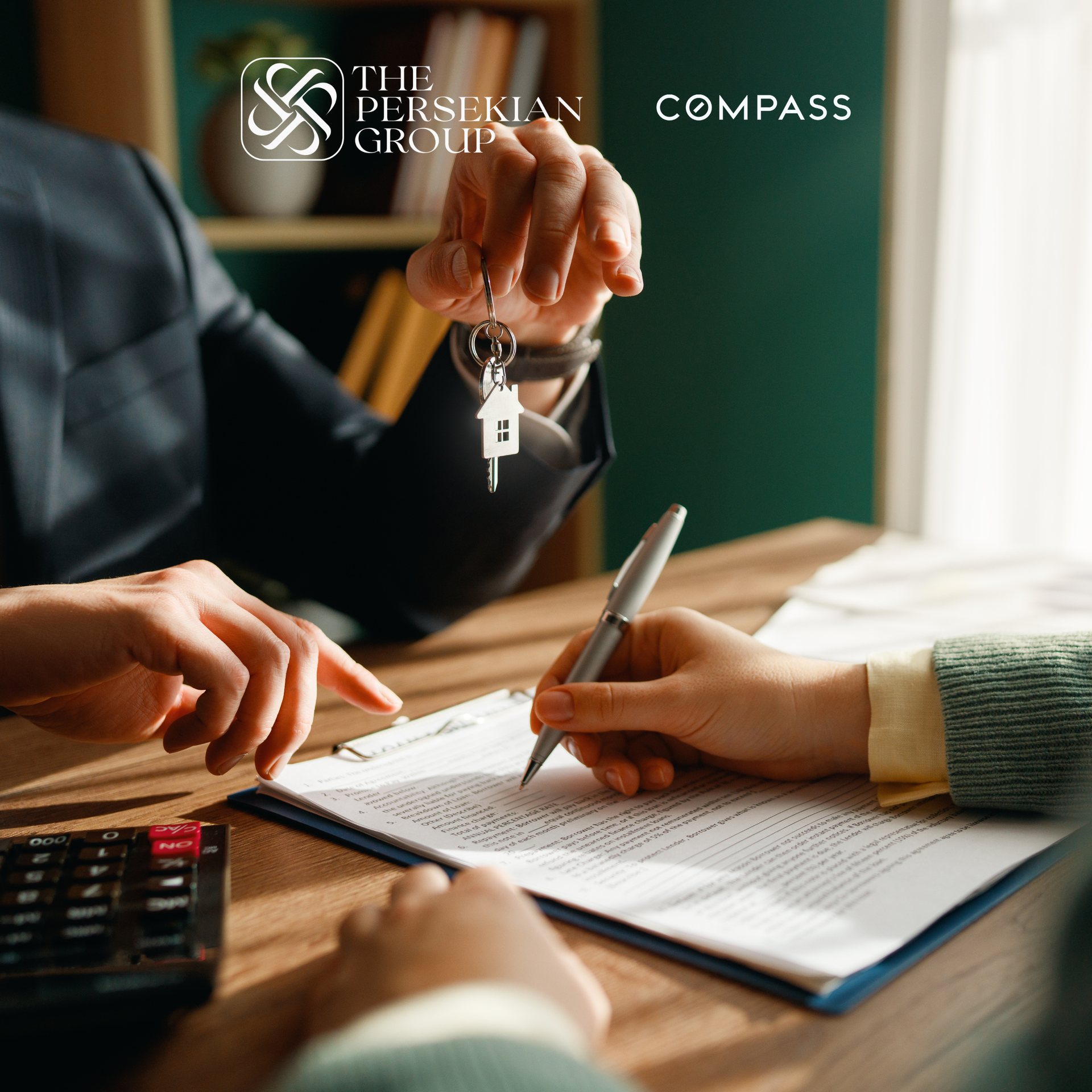 A person handing over house keys to a someone signing documents at a desk.