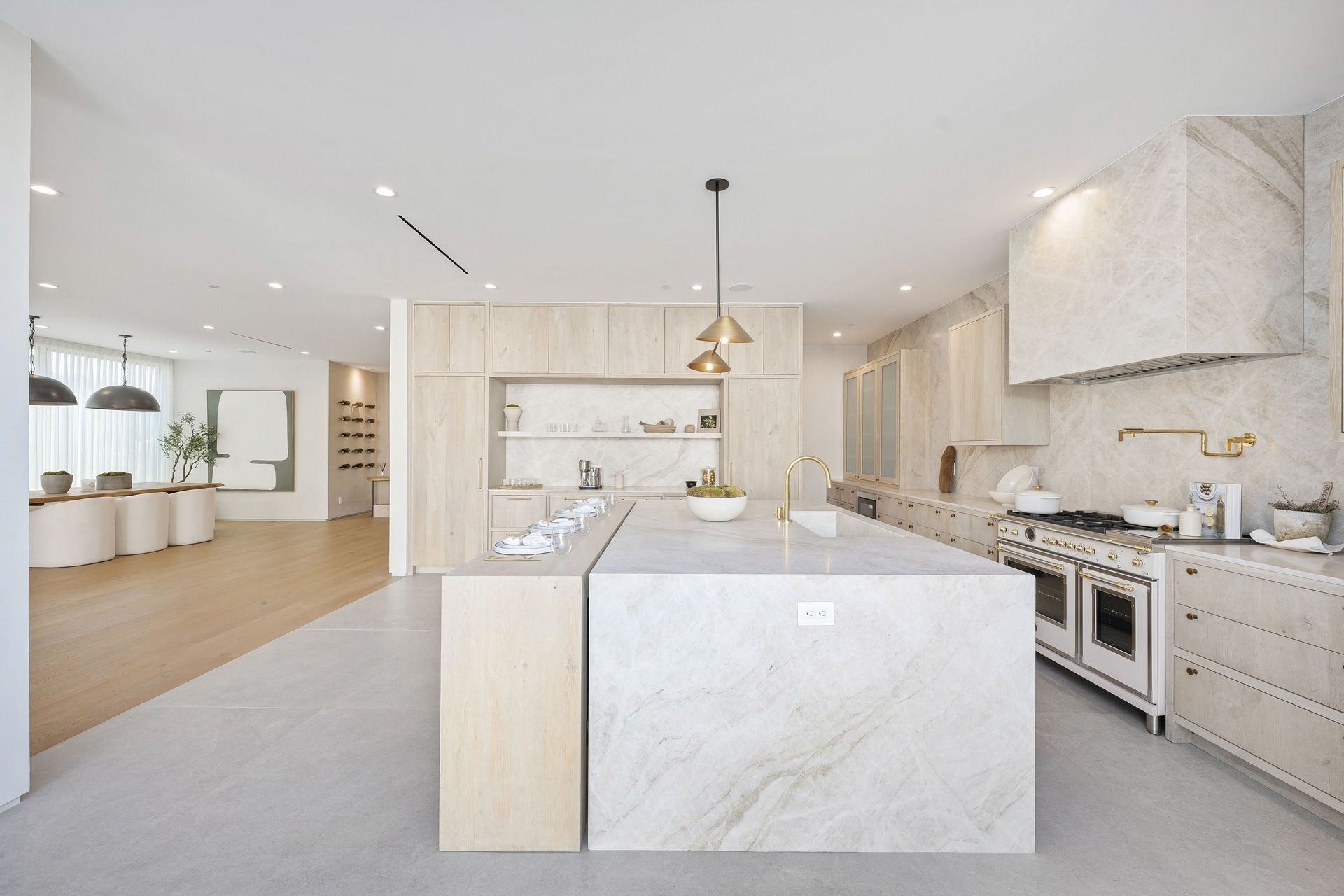 Bright white kitchen with marble waterfall island, stainless steel appliances, and pendant lights.