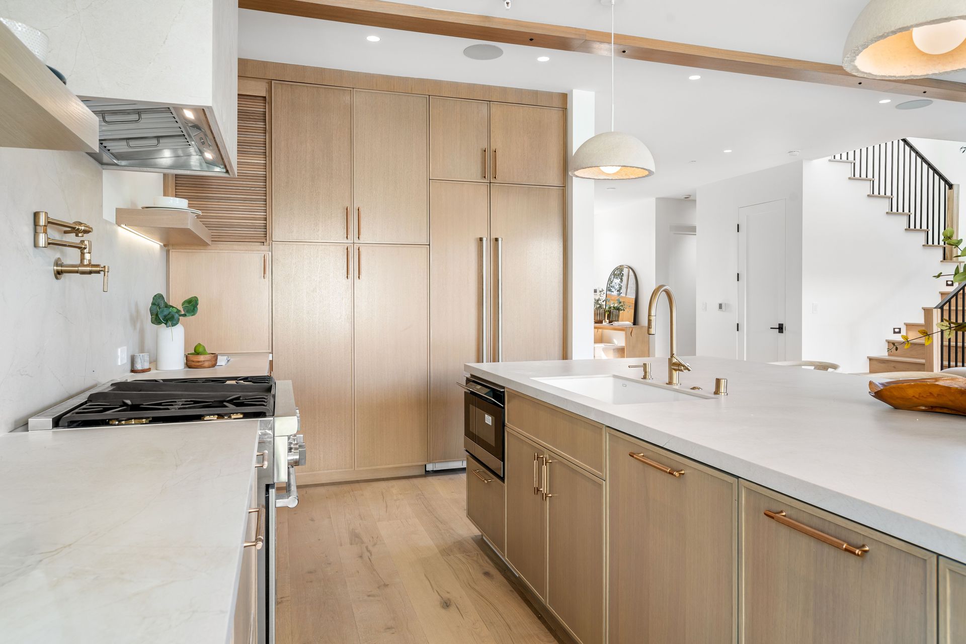 Modern kitchen with floor-to-ceiling wood cabinets, marble countertops, and staircase view.