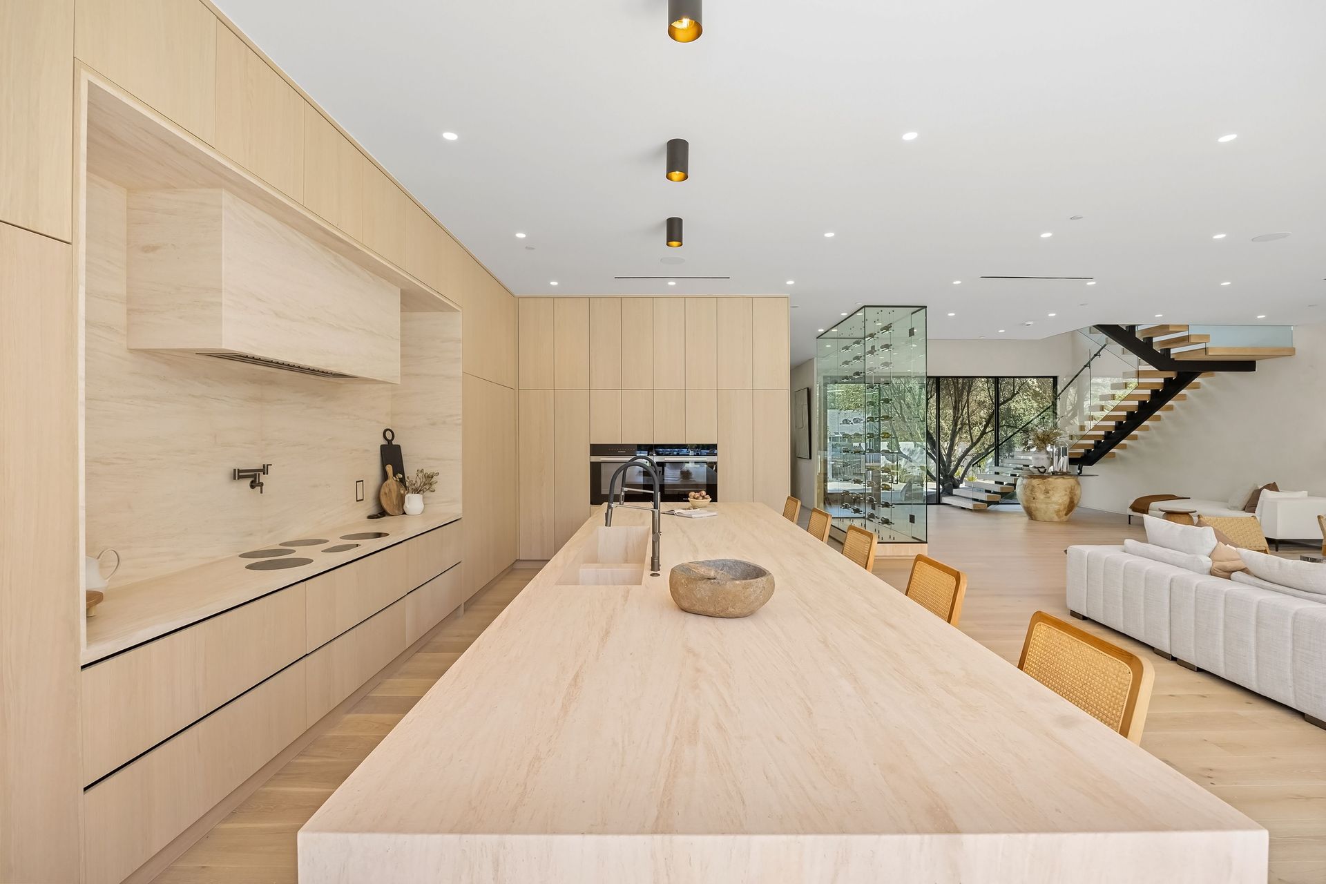 Kitchen hallway with wood cabinetry, herringbone flooring, and large window overlooking greenery.