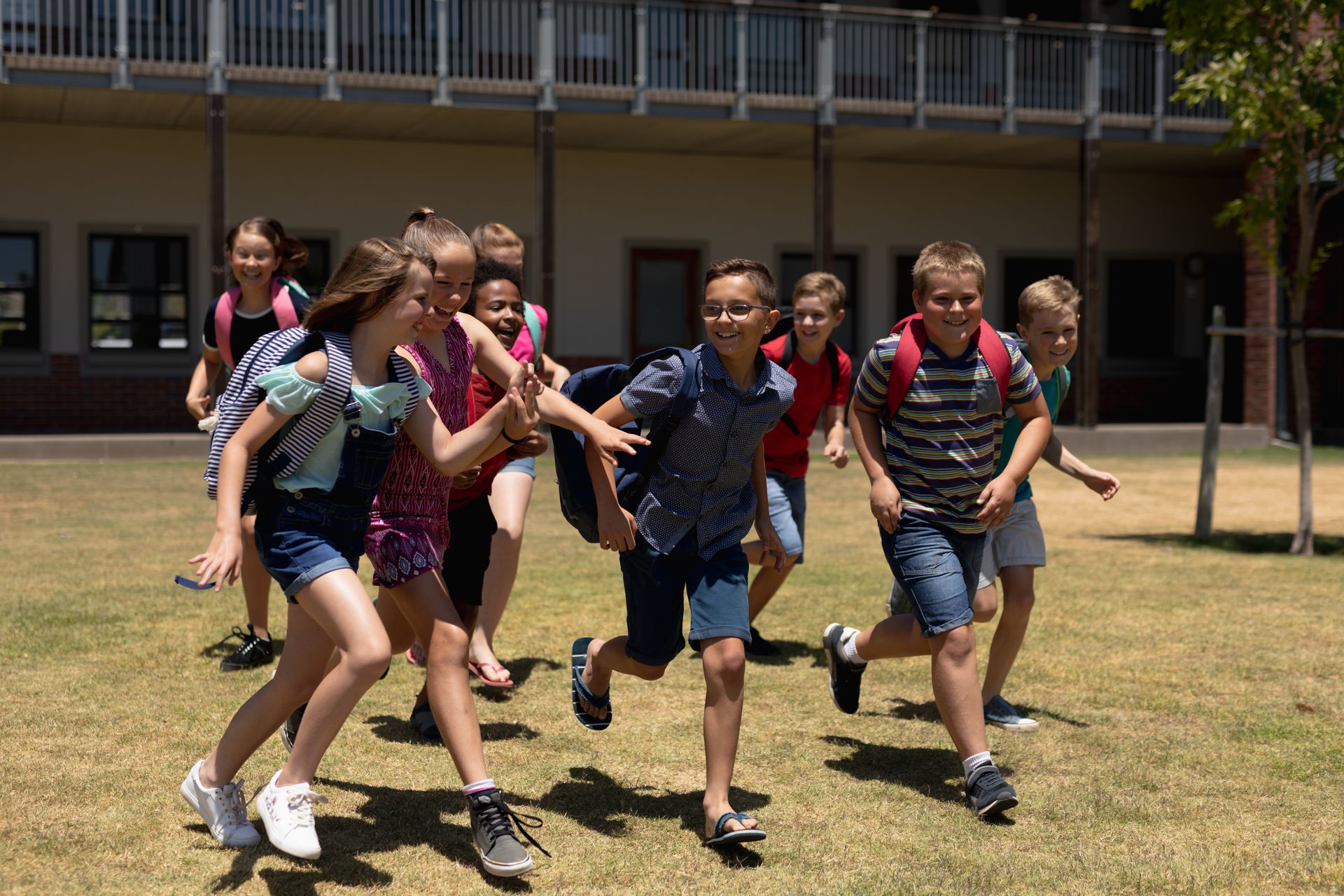 Group of children running and laughing outdoors on a school campus on a sunny day.