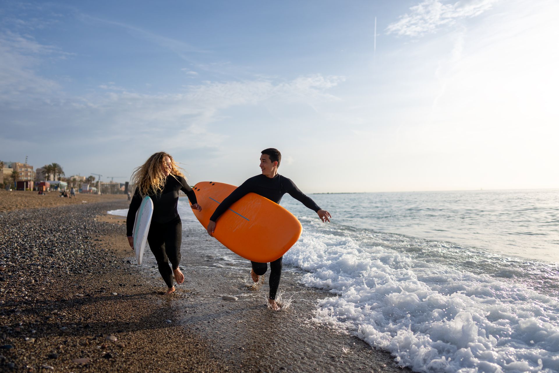 Two people carrying a surfboard along the San Clemente shoreline with waves in the background.