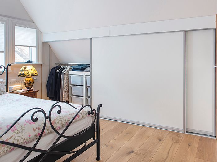Helles Schlafzimmer mit schwarzem Metallbett, Dachschräge, Holzboden und Schiebetüren zum Kleiderschrank.