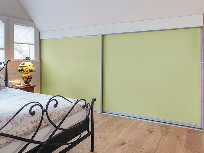 Schlafzimmer mit hellgrünen Schiebetüren zum Kleiderschrank, Holzboden und einem schwarzen Metallbettgestell.