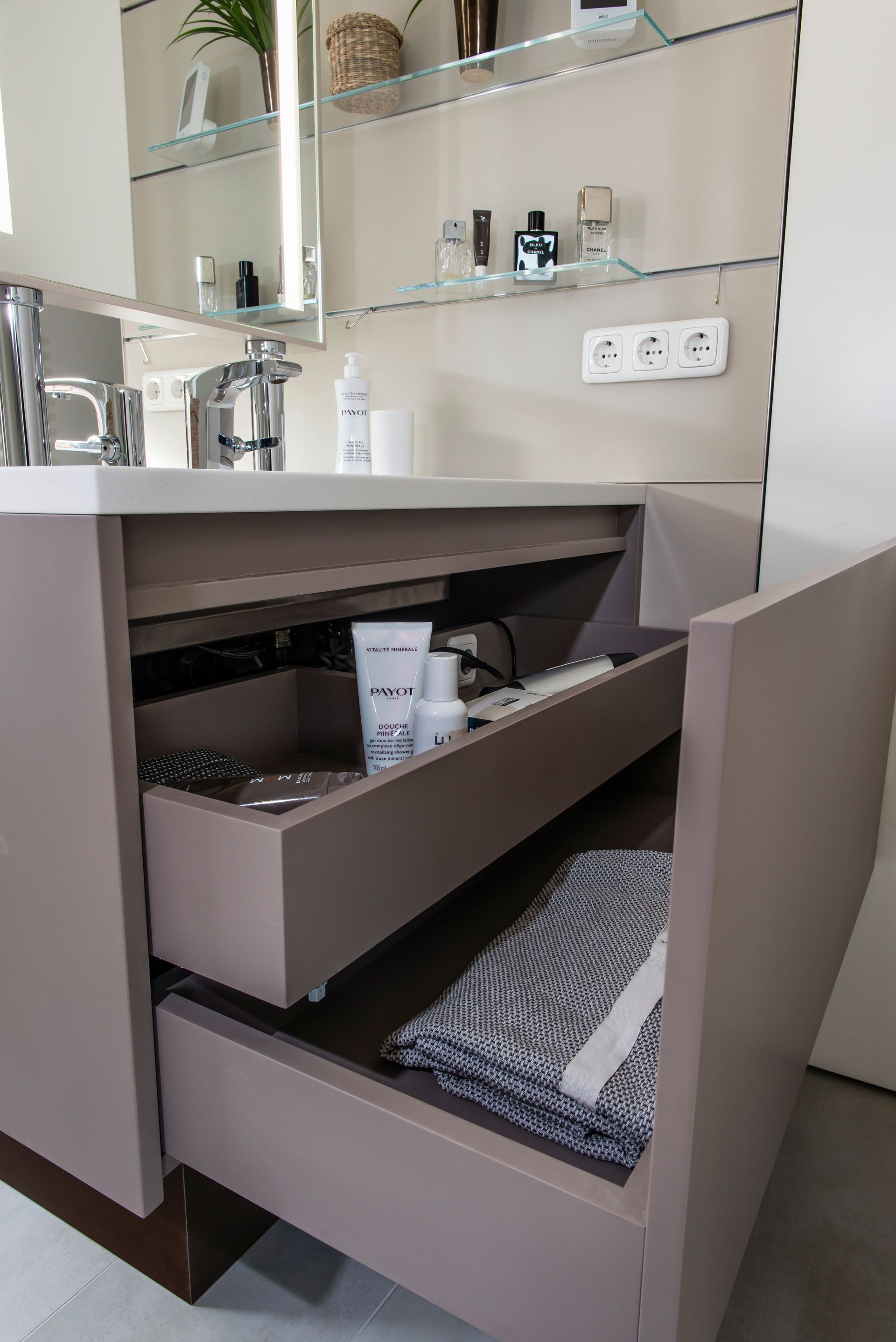 Badezimmerschrank mit offener Schublade für Toilettenartikel und gefaltete Handtücher unter einem Waschbecken 