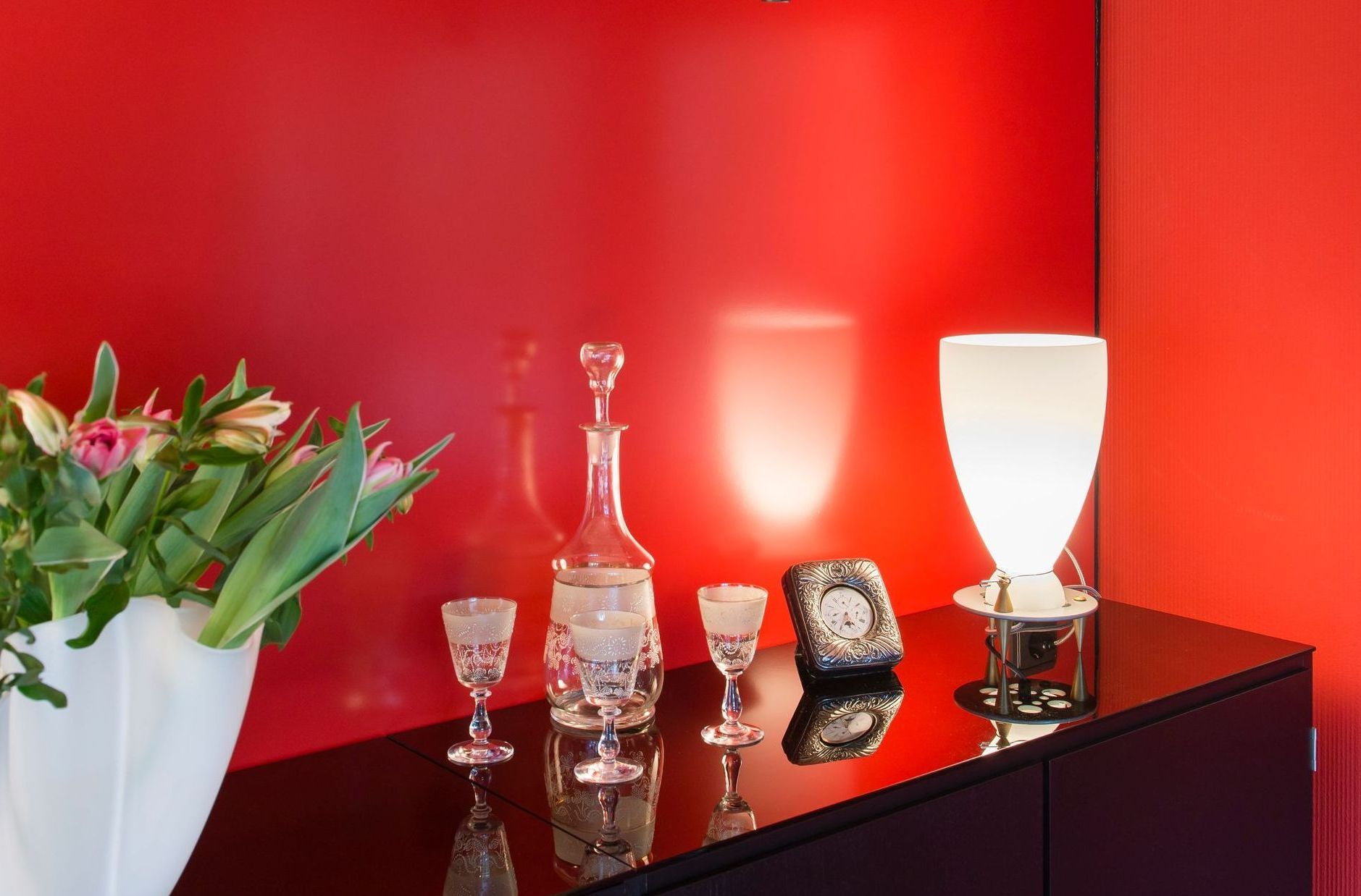 Modernes rotes Zimmer mit Glasschrank, weißer Lampe und Blumen auf glänzend schwarzem Untergrund
