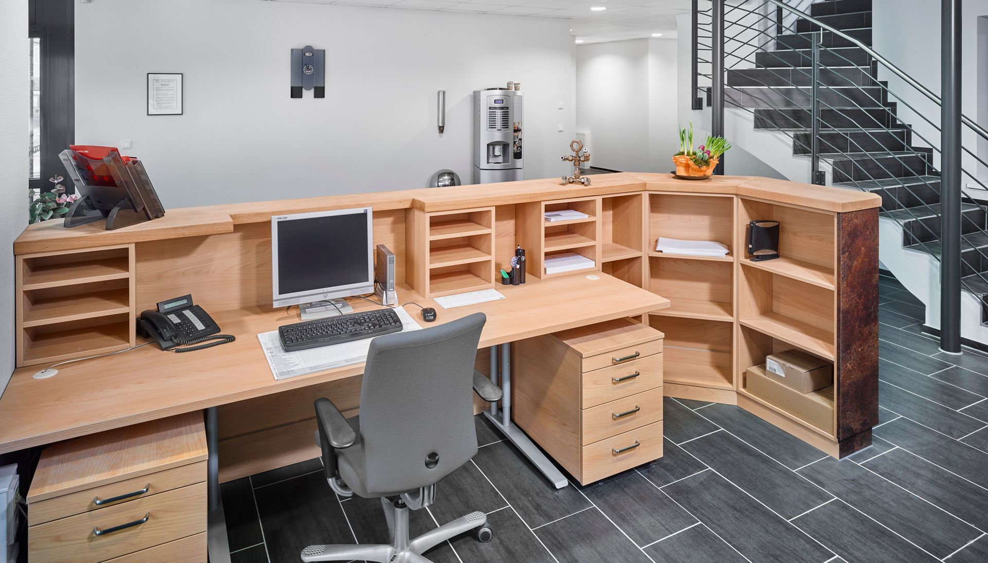 Empfangstresen aus Holz mit Computer, Stuhl, Schubladen und Regalen in einer hellen Bürolobby