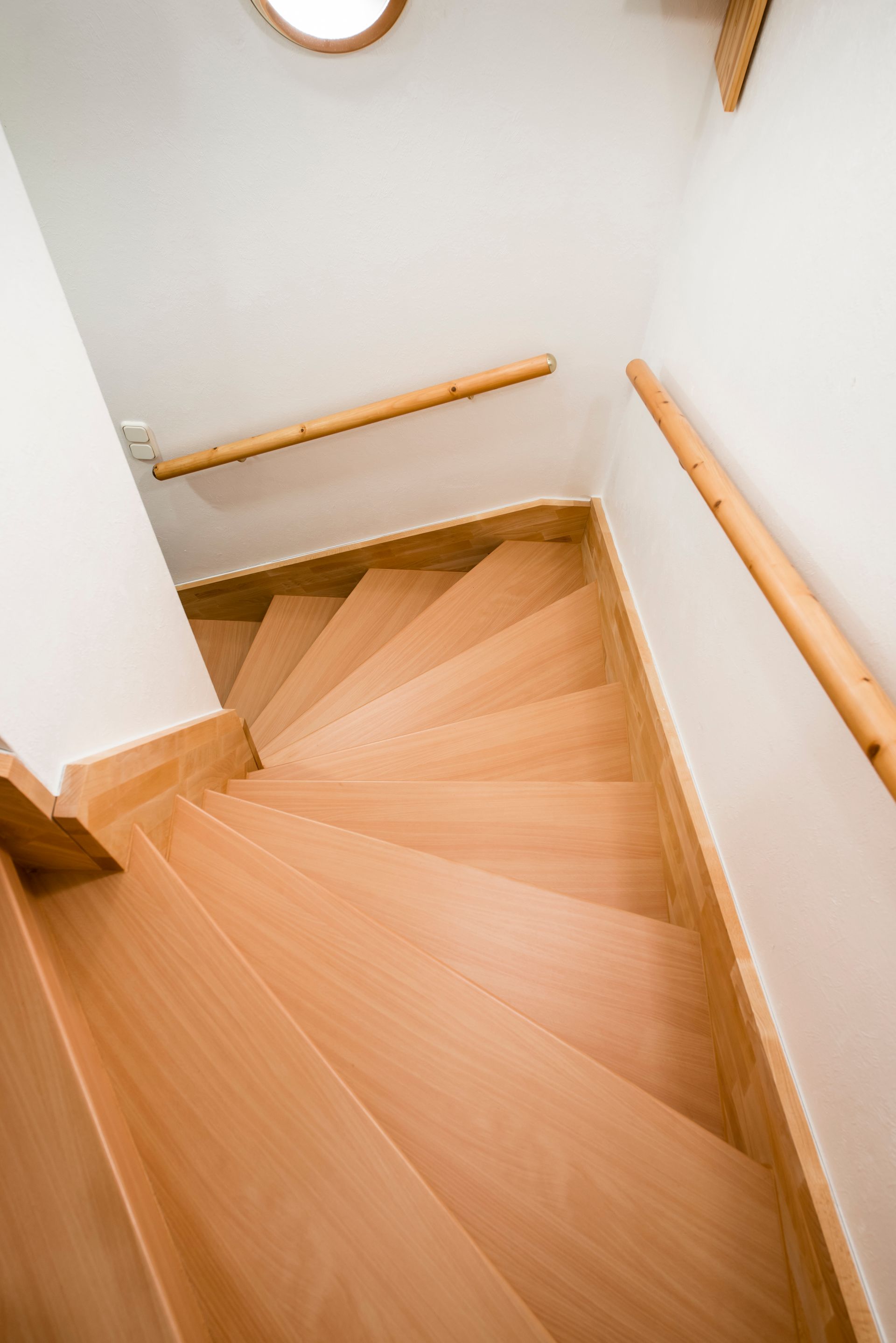 Draufsicht auf eine helle Holztreppe mit weißen Wänden und Holzgeländern.