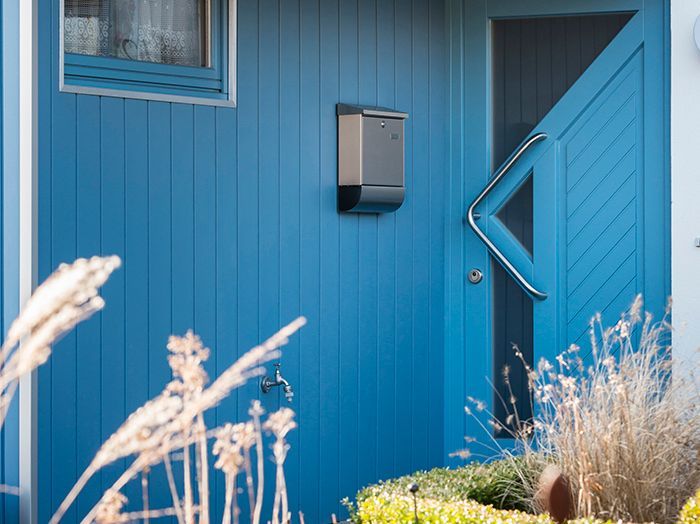 Eingang zum blauen Haus mit Tür, Briefkasten, Fenster und trockenem Gras im Vorgarten
