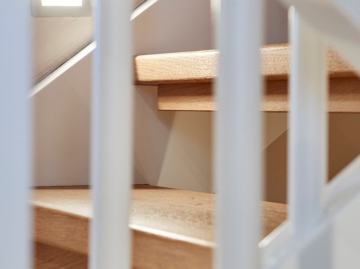Holztreppe, durch weiße Treppengeländer in einem sanft beleuchteten Innenraum sichtbar