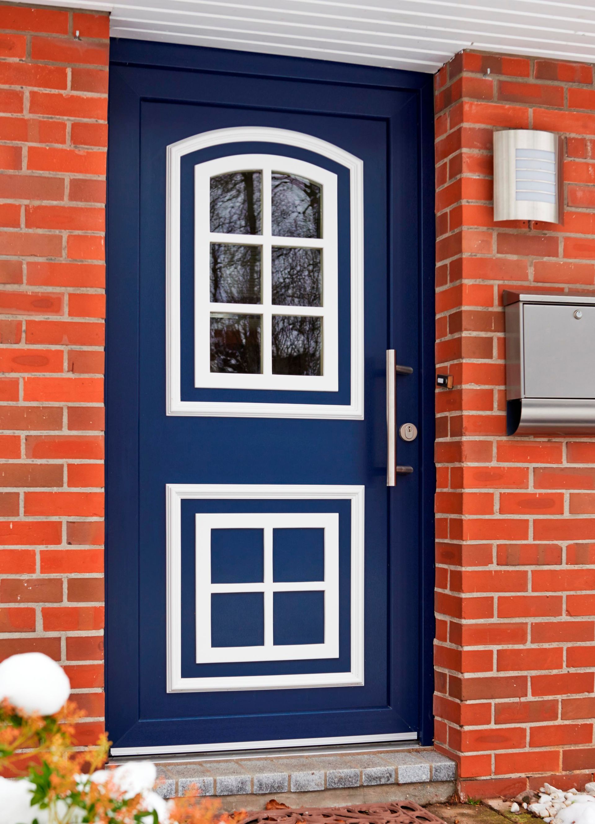 Blaue Haustür mit weißen Zierleisten und Fensterflügeln, eingefasst in eine rote Backsteinmauer