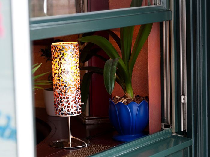 Bunte Lampe und blaue Topfpflanze auf einem Fensterbrett hinter einem grün gerahmten Fenster