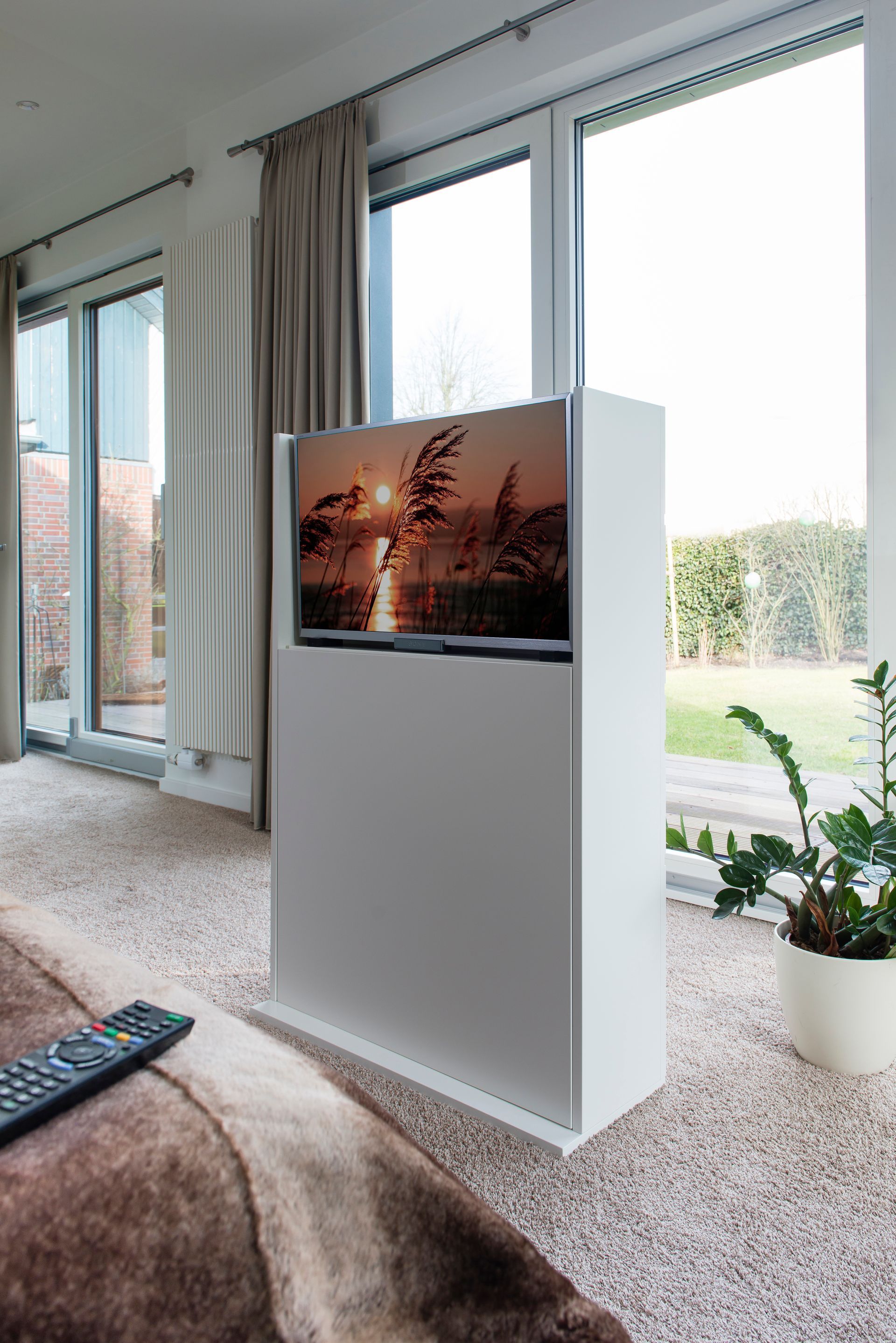 Modernes Wohnzimmer mit großem weißen Kamin oder TV-Konsole vor hellen Fenstern und Vorhängen.