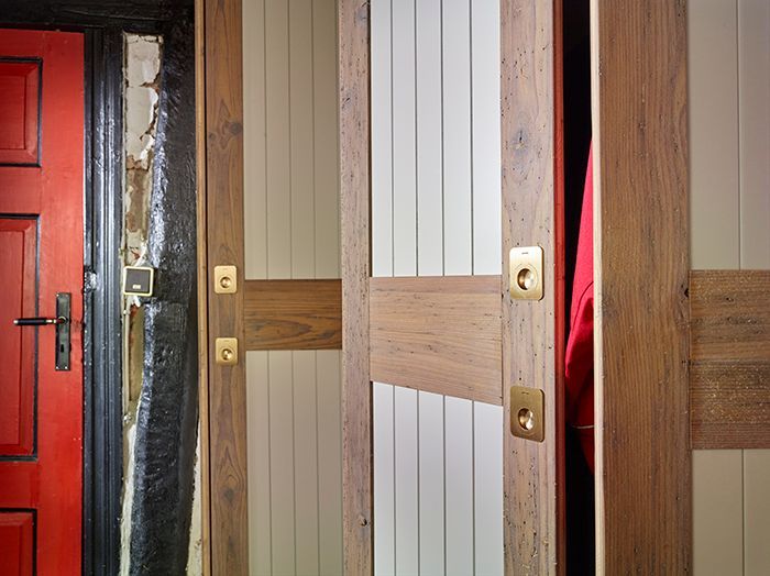 Holztüren von Toilettenkabinen, eine davon teilweise geöffnet, innen ist ein rotes Tuch zu sehen.