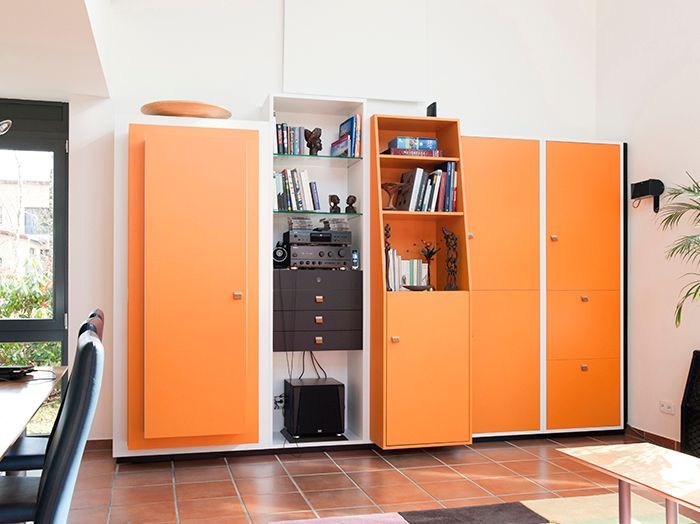 Orangefarbene Aufbewahrungsschränke in einem Raum mit Regalen, Elektronikgeräten und einem Fenster auf der linken Seite.