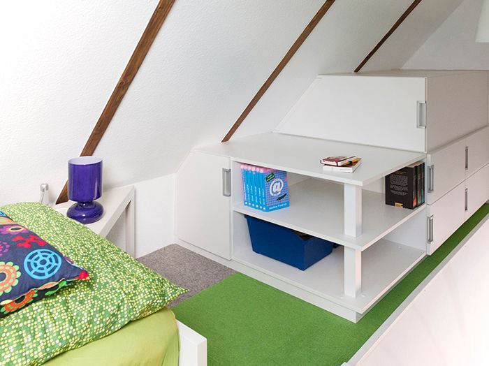 Loft-Schlafzimmer mit weißem Regal, grünem Teppich und farbenfroher Bettwäsche unter Dachschräge.