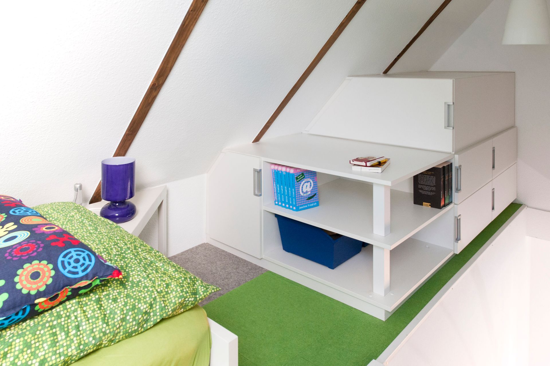 Helles Dachgeschoss-Schlafzimmer mit grüner Bettwäsche und einer weißen Hochbettnische mit Regalen und blauen Akzenten