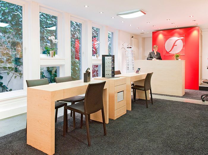Modernes Optiker-Interieur mit Beratungsplätzen, Spiegeln, Stühlen und einer roten Akzentwand