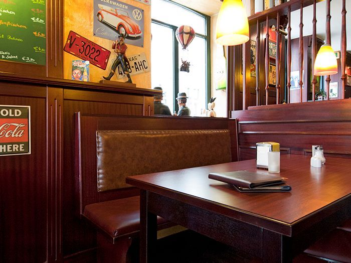 Gemütliche Restaurantnische mit Holztisch, Pendelleuchten und Wandbildern am Fenster