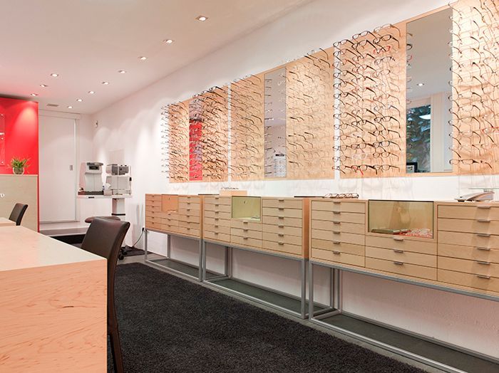 Modernes Ladeninterieur für Optiker mit wandmontierten Brillengestell-Auslagen und Holzschränken.