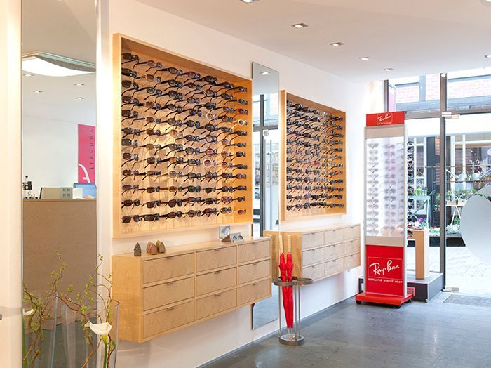 Innenansicht eines Optikergeschäfts mit Wanddisplays von Brillenfassungen und einem roten Ray-Ban-Präsentationsständer