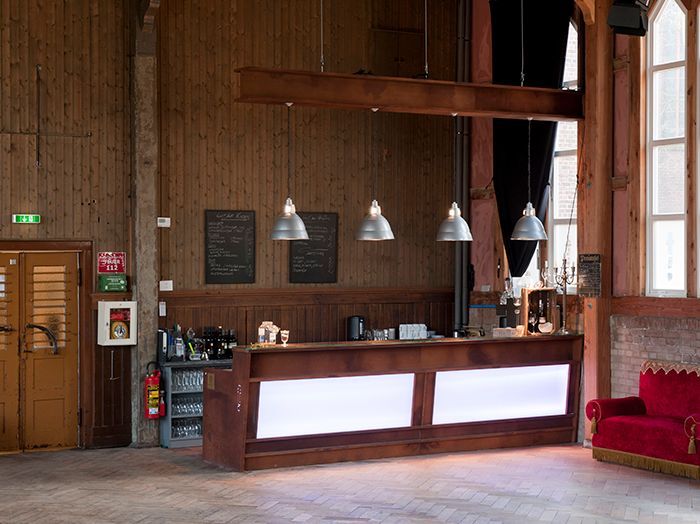Holzgetäfelte Lobby mit hölzernem Thekentresen, Hängelampen und einem roten Sofa an hohen Fenstern.