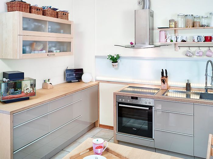 Moderne Küche mit hellen Holzschränken, Edelstahlbackofen, offenen Regalen und einem Spülbeckenbereich
