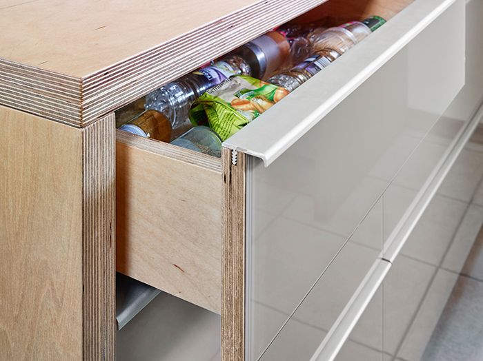 Offene Schublade mit ordentlich sortierten Snackpäckchen in einem Holzschrank neben einer glänzend weißen Wand