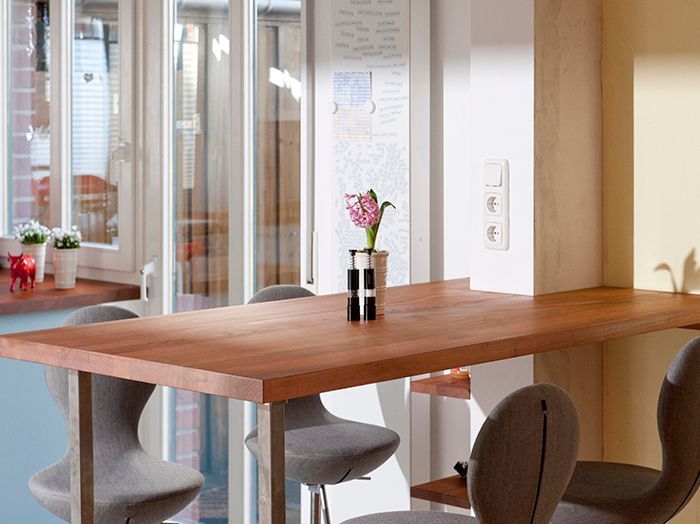Modernes Esszimmer mit Holztisch, grauen Stühlen und einer kleinen Blumenvase neben den Glastüren.
