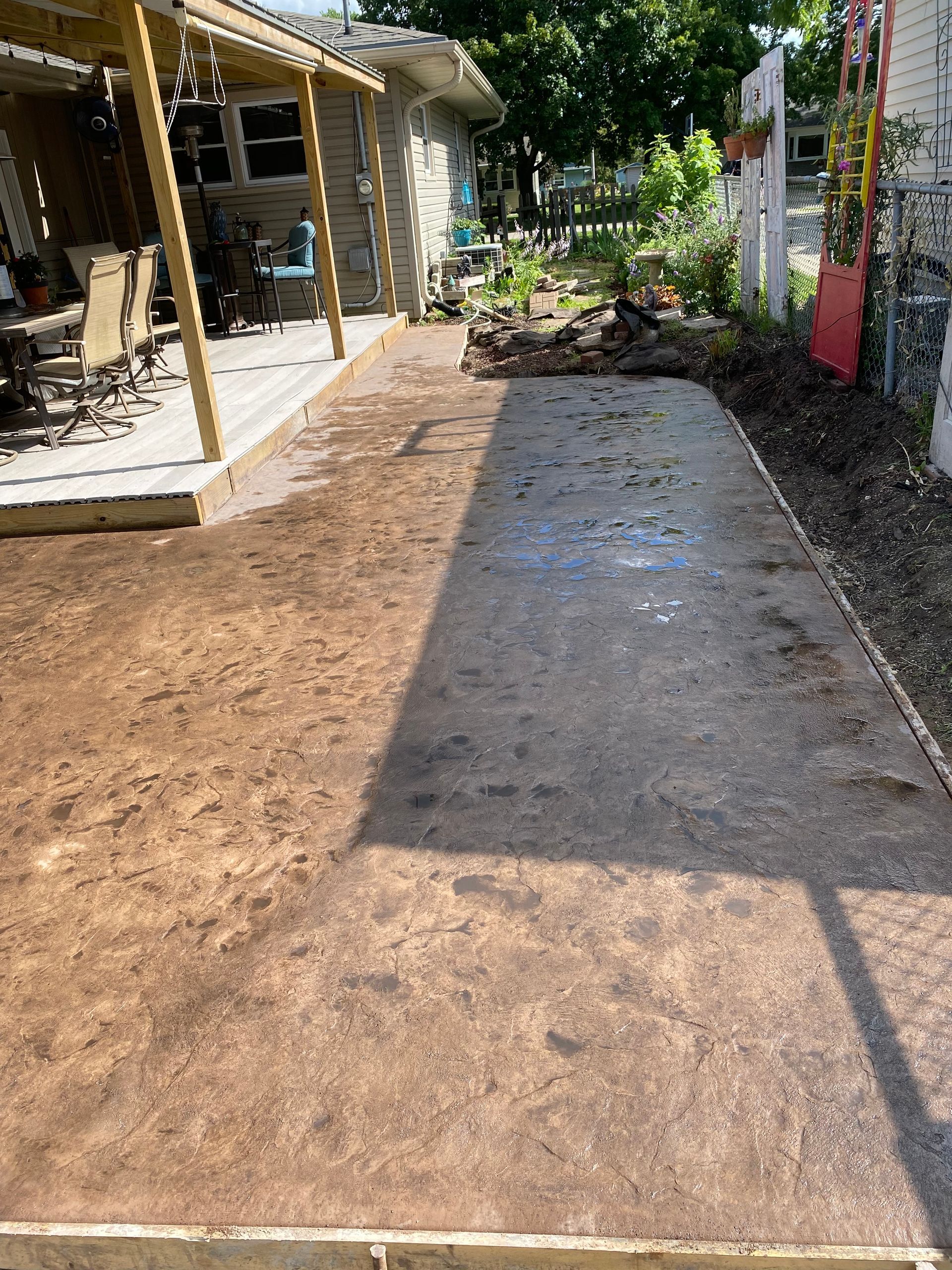 A concrete driveway is being built in a backyard next to a house.