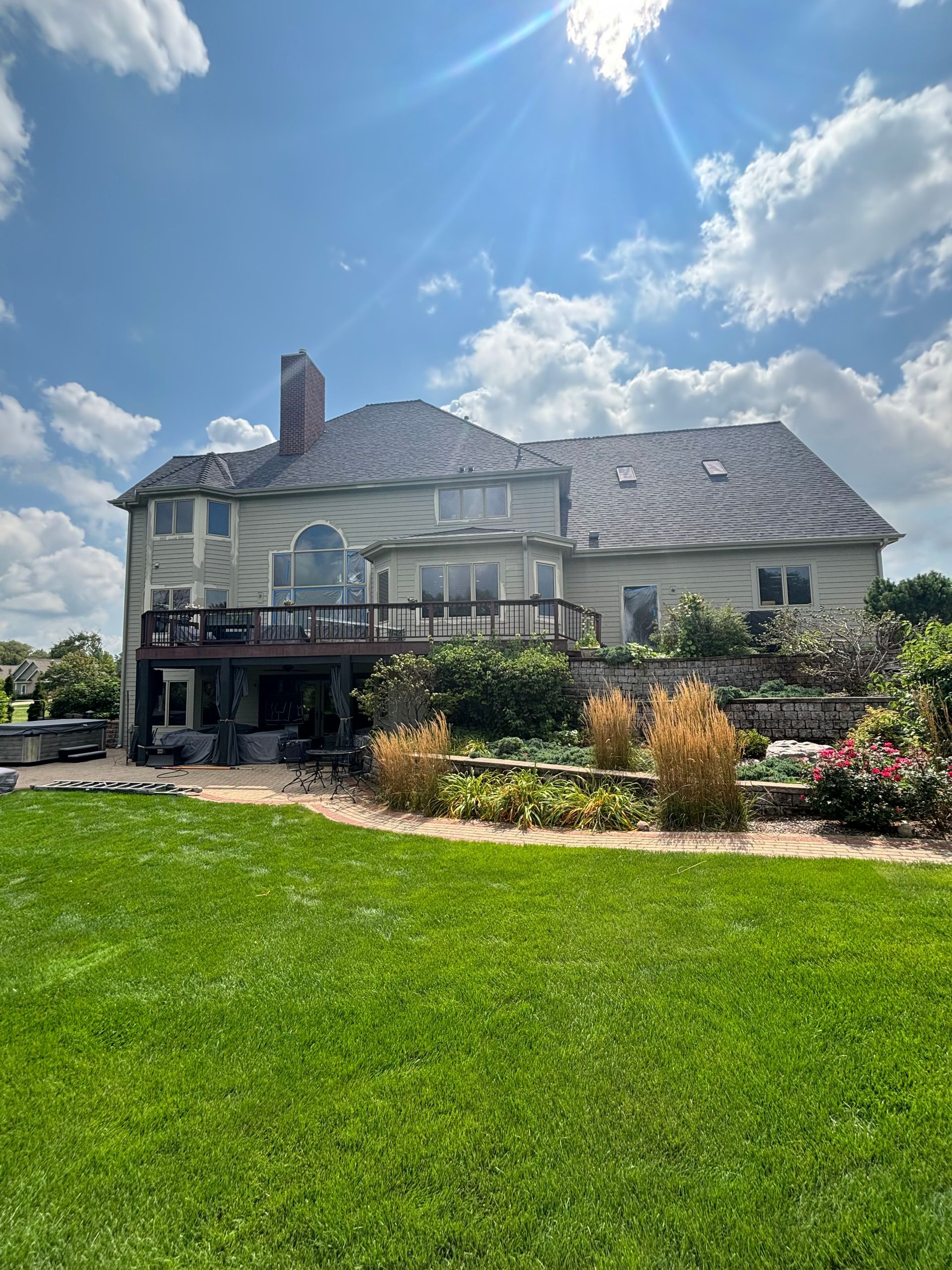 Rear view of a Janesville, Wisconsin home with new gutters above a deck and landscaped backyard.