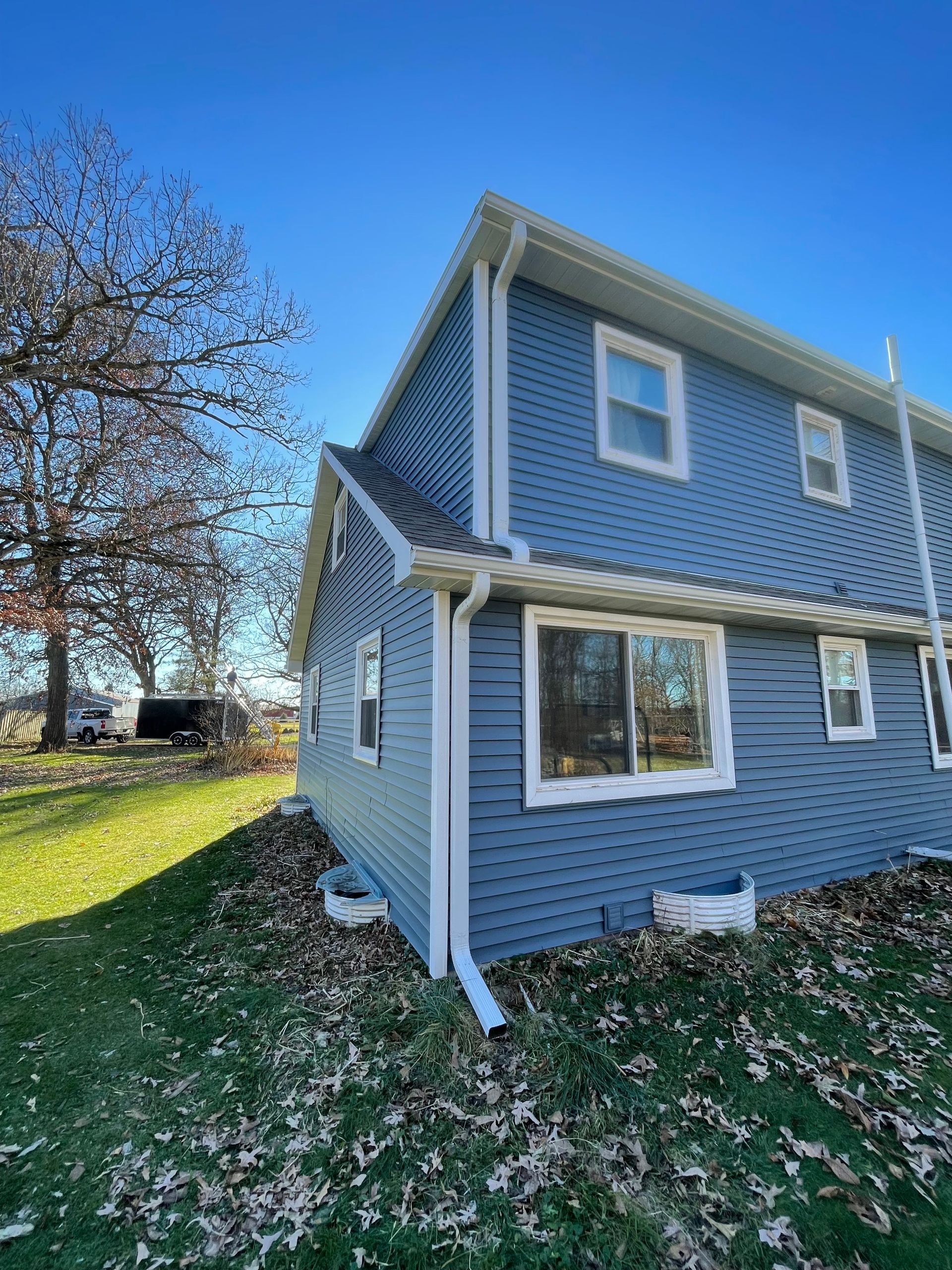 A blue house with white siding and windows is sitting on top of a lush green hill.