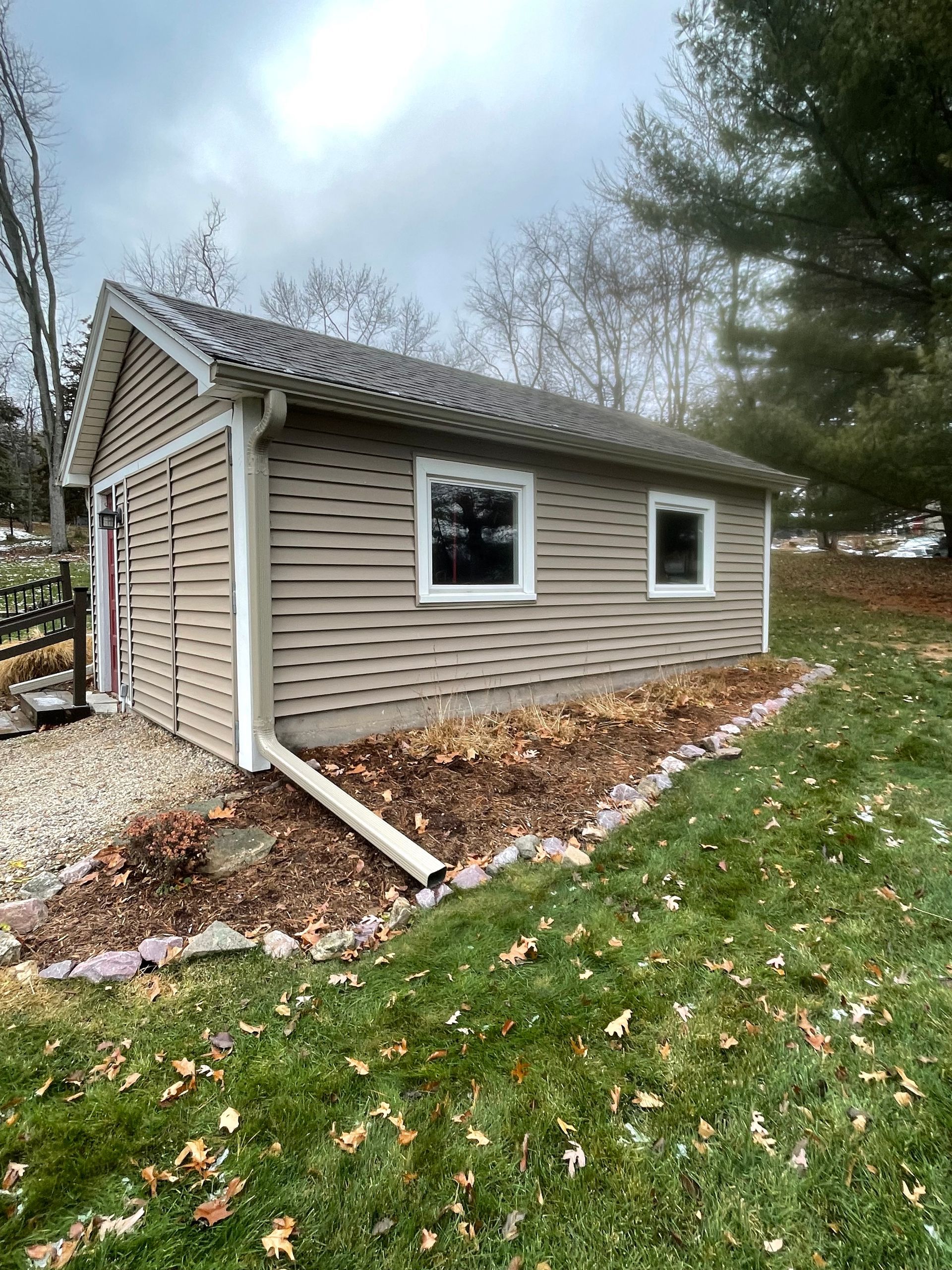 A garage with siding and windows is sitting in the middle of a lush green field.