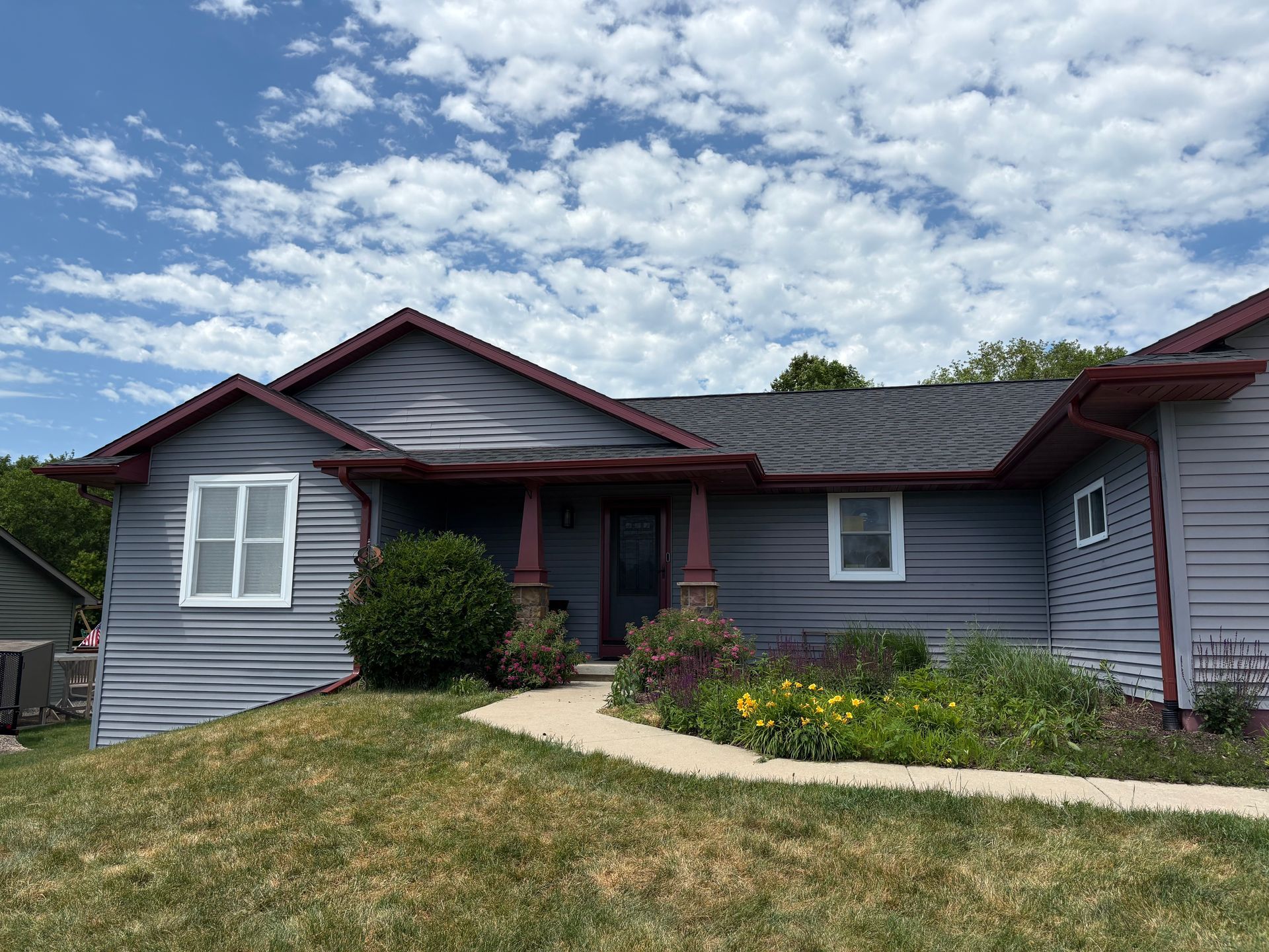 Gray house with red trim, green lawn, blue sky with white clouds.
