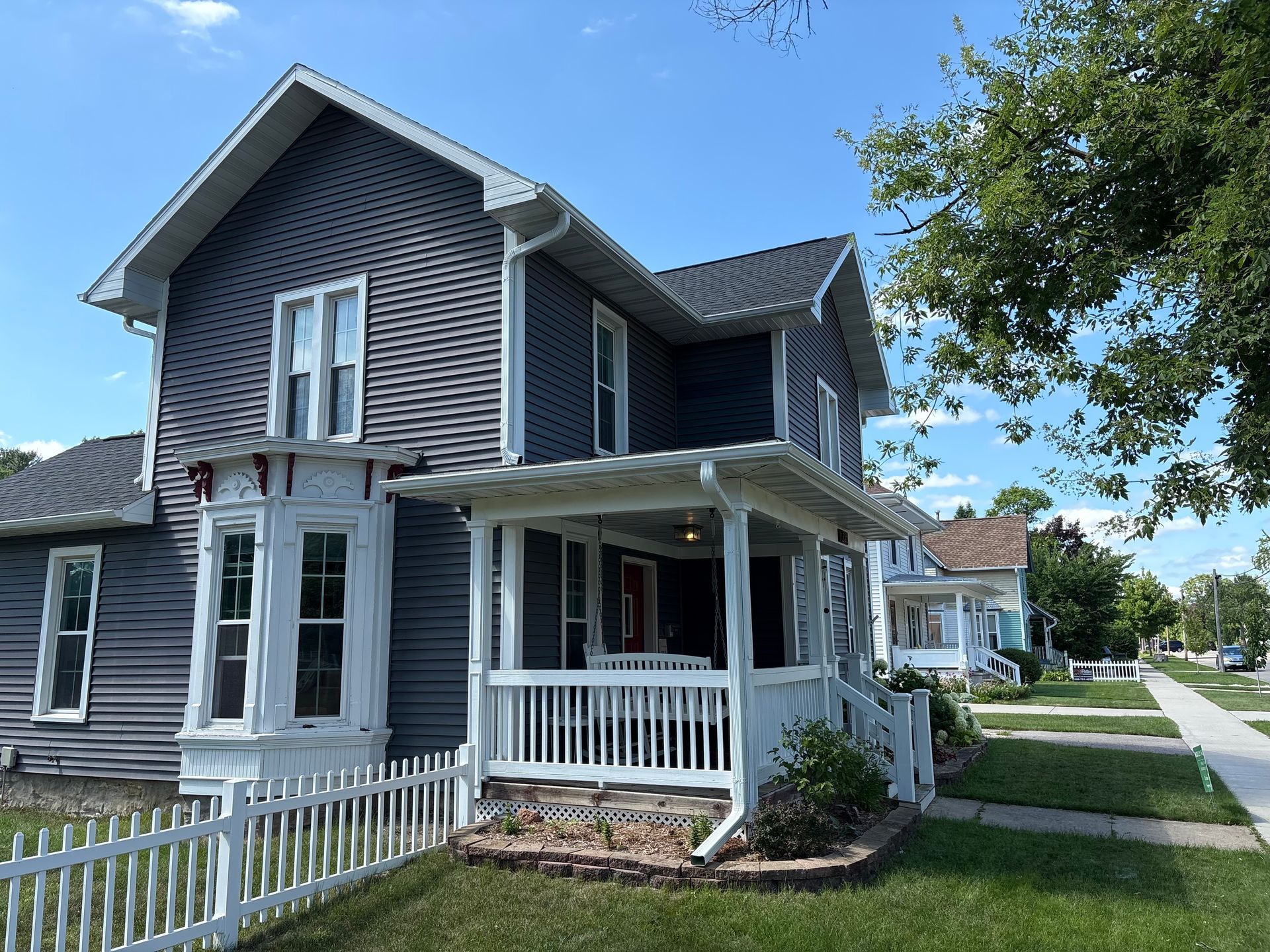 Side view of a Madison, WI home with newly installed white gutters and downspouts around a covered porch.