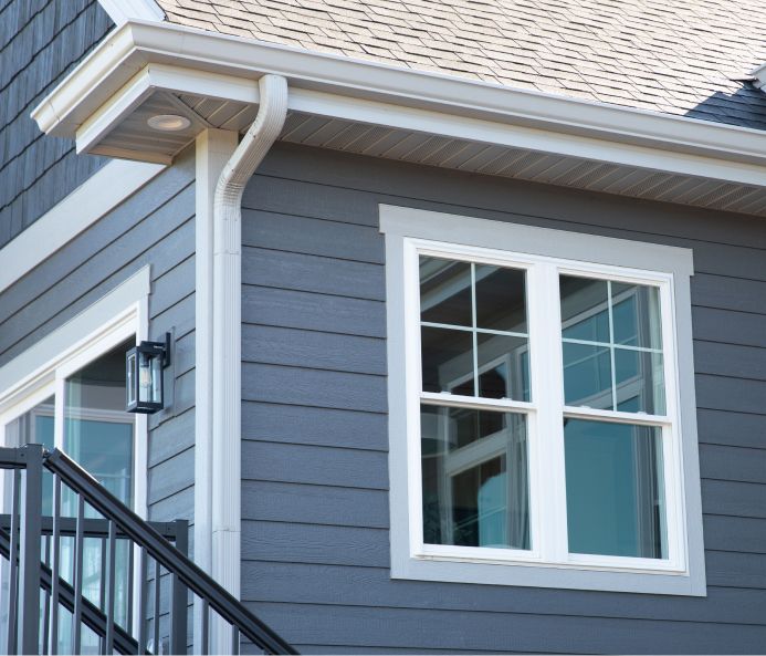 Blue-gray house exterior with white trim, gutters, and window frame; black stair railing.