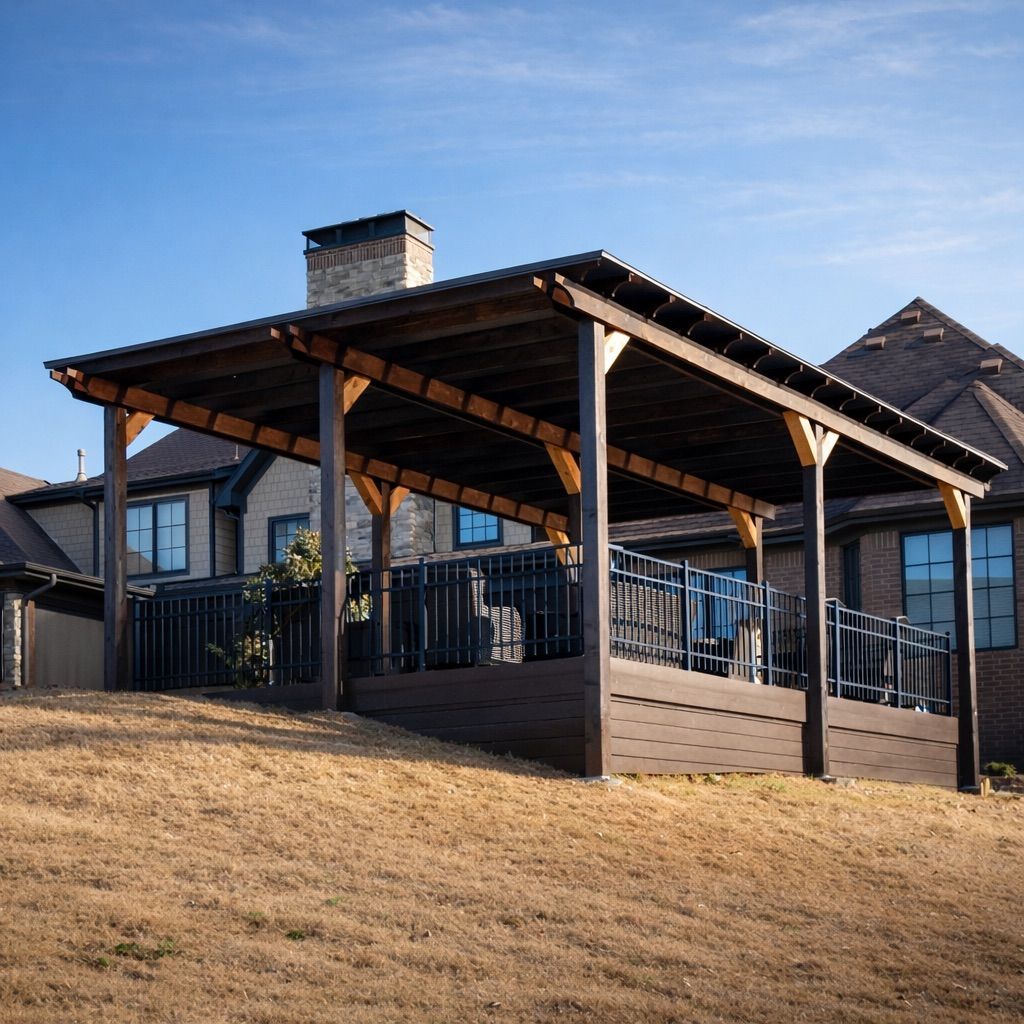 Covered wooden deck with railing on a sloped yard beside a house under a blue sky