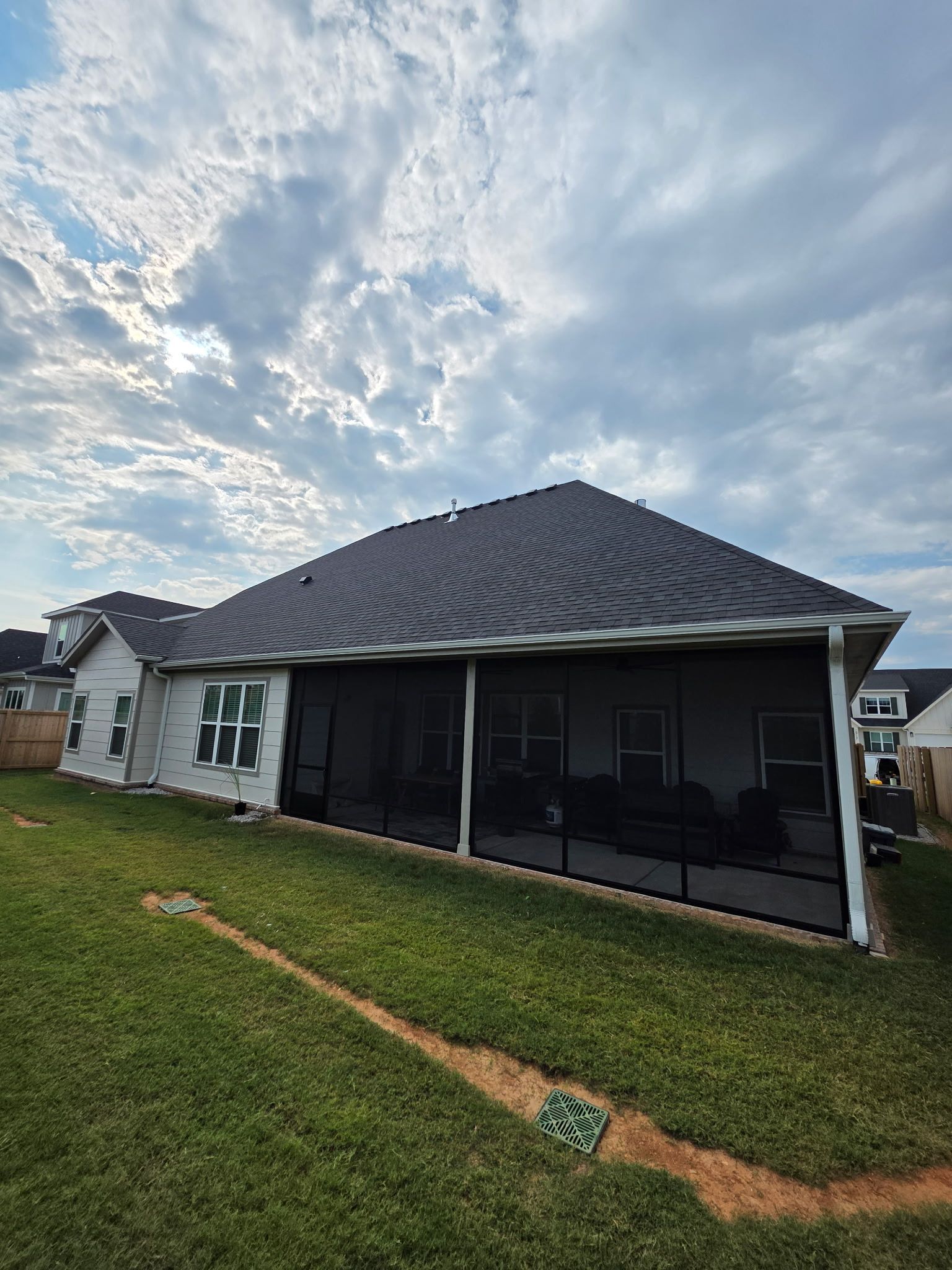 Single-story house with a dark gray roof, screened porch, and grassy yard under a cloudy sky.
